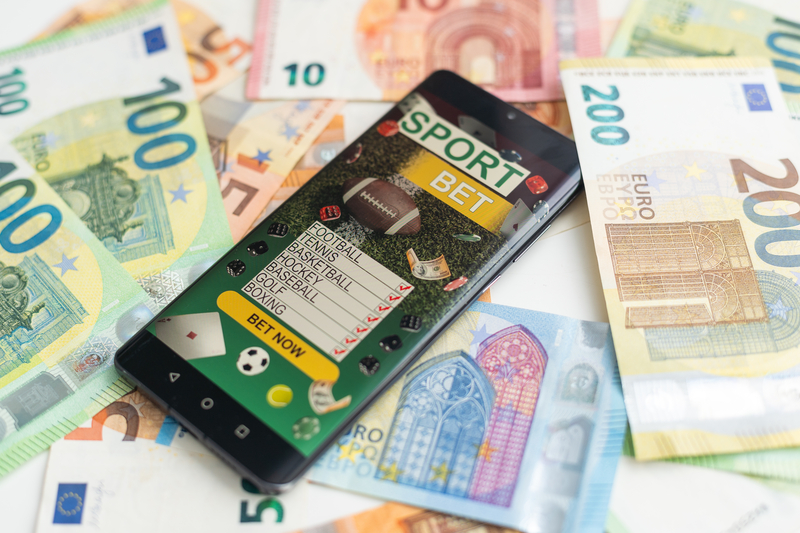 Sportwetten-App auf Smartphone, Euro-Geldscheine im Hintergrund