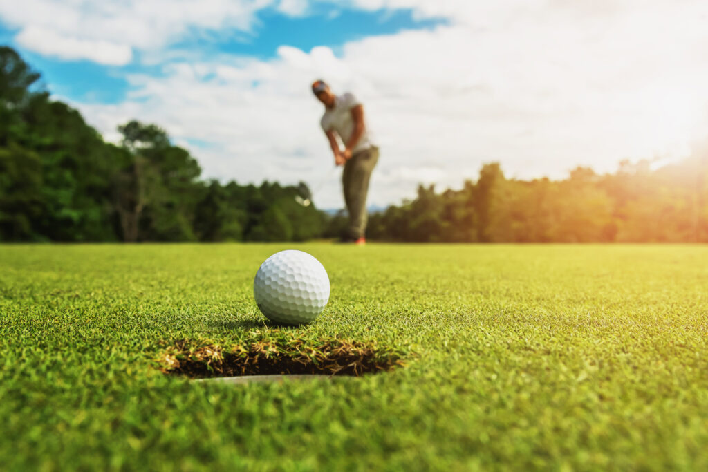 Golfer hits ball on green in sunshine